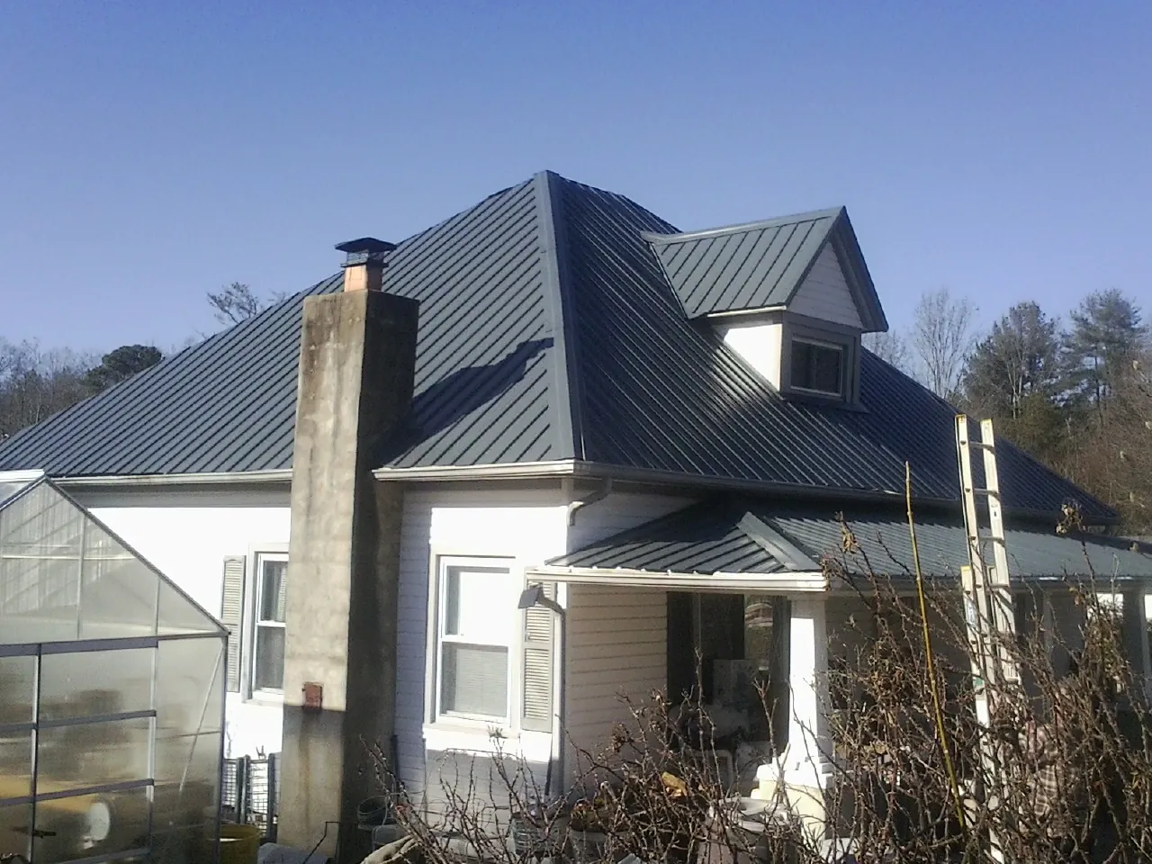Dark blue standing seam metal roof on a white farmhouse with dormer — Slate & Tile Roof Repair by Roofing Brothers in Mosby