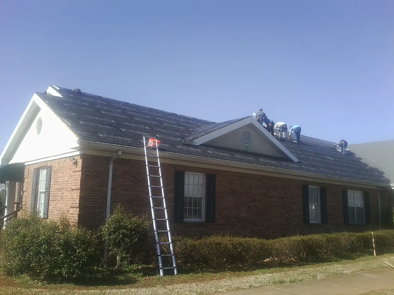 Crew tearing shingles off a brick ranch roof with a ladder set — Emergency Roof Repair work by our crew in Mosby