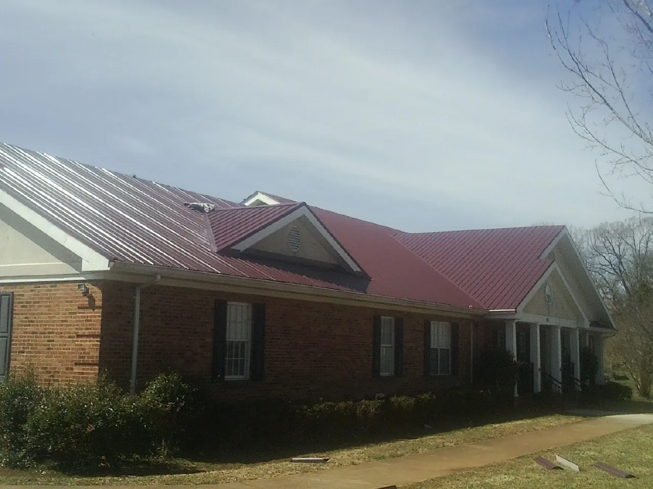 Red metal roof with gabled entries on a long brick building, from a Hail Damage Roof Repair job in Mosby
