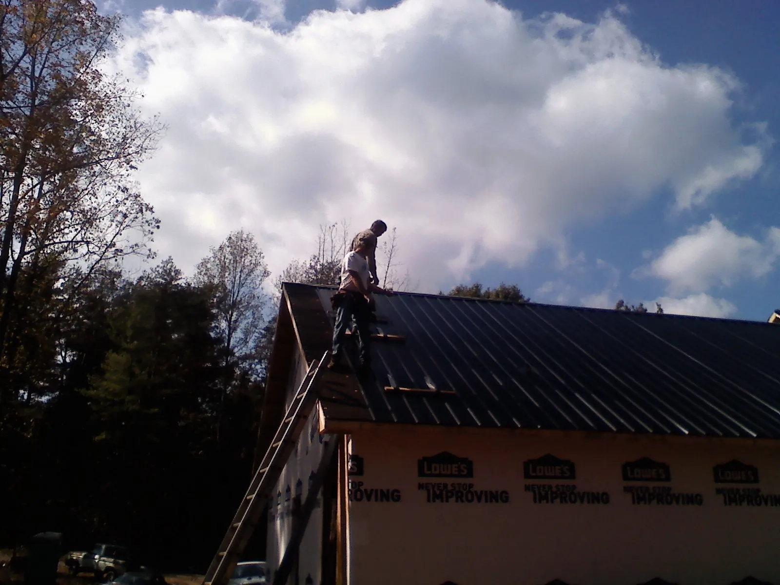 Roofer fastening dark metal panels high against a cloudy sky, from a Roof Inspection job in Mosby