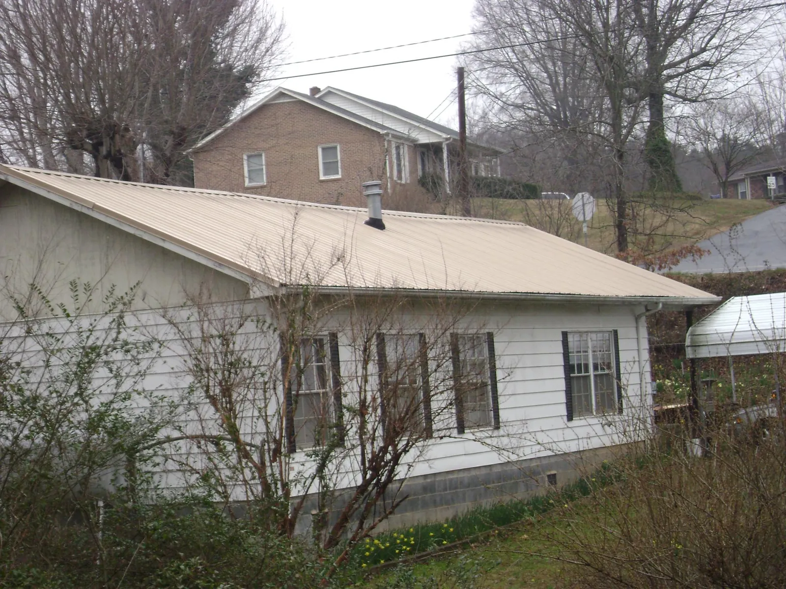 Tan metal roof on a white sided house set into a hillside — Commercial Roofing by Roofing Brothers in Mosby